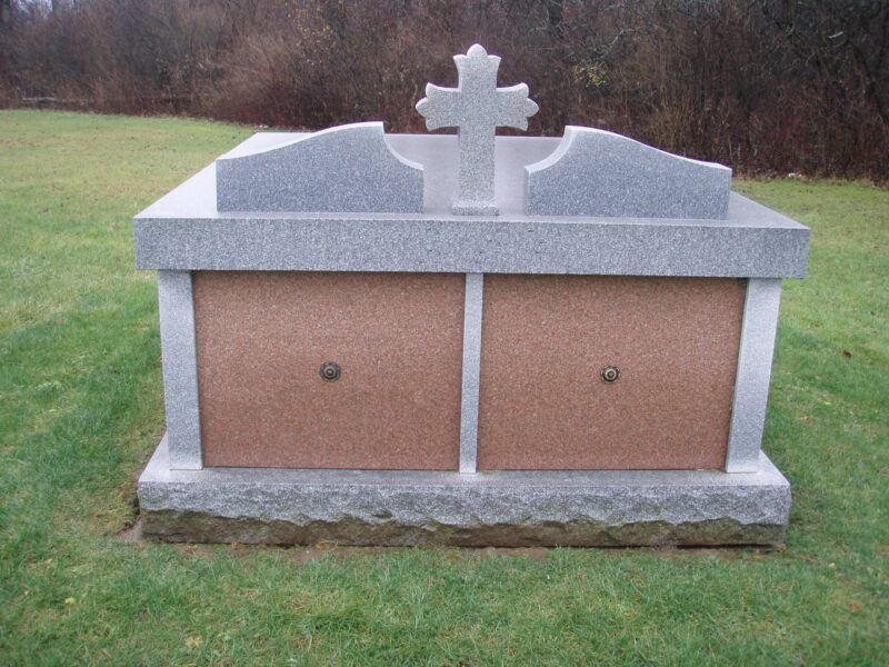 A grave with two doors and a cross on top.