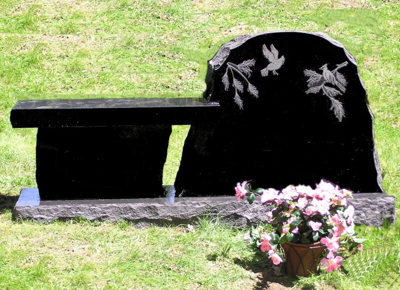 A black grave with flowers in the background.